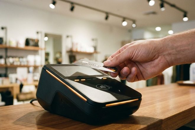 Hand houdt contactloze betaalkaart boven moderne RFID-terminal op houten toonbank in winkel
