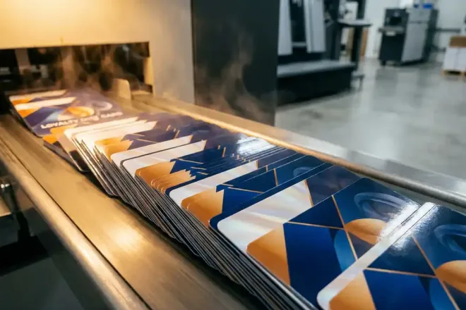 Stapel glanzende loyaliteits- en cadeaukaarten op transportband van industriële drukpers, warm goudkleurig licht op kaartoppervlak.