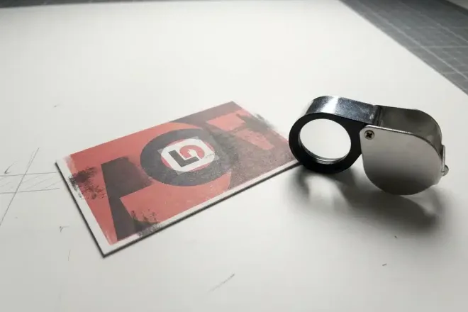 Afgewezen loyaliteitskaart met kleurmisdruk op witte productietafel, naast een kwaliteitscontroleloepe, studioverlichting.