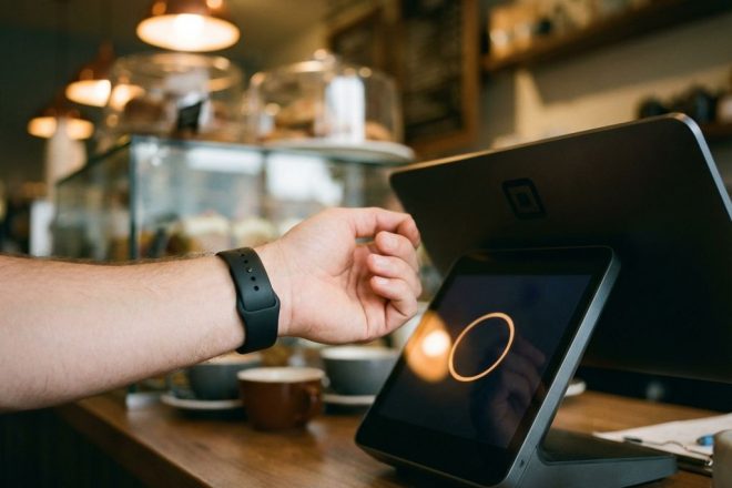 Persoon met zwarte RFID-polsband maakt contactloze betaling bij koffieshop kassasysteem