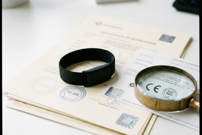 Zwarte RFID-polsband op certificeringsdocumenten met vergrootglas over kwaliteitsmerken en compliance badges