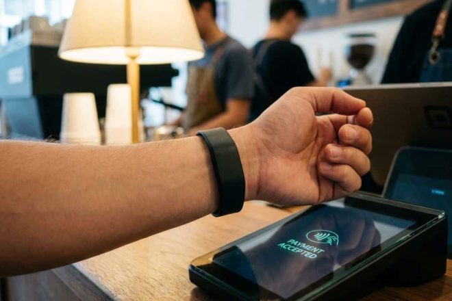 Persoon met zwarte RFID-polsband maakt contactloze betaling bij koffieshop terminal