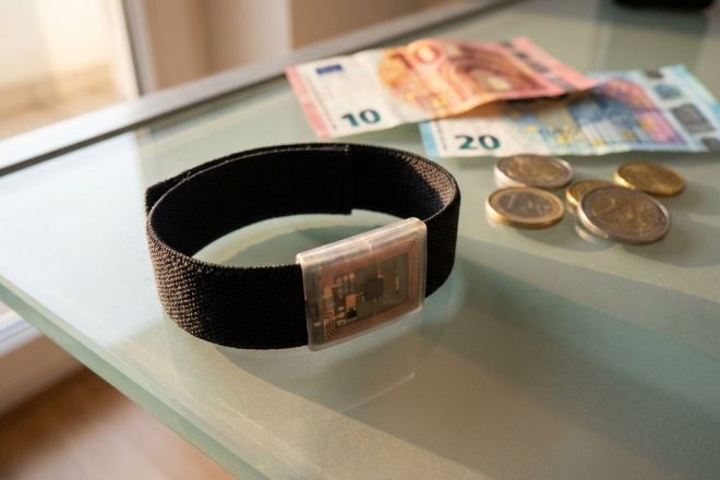 Zwarte RFID-polsband met zichtbare chip op glazen bureau naast Europese bankbiljetten en munten