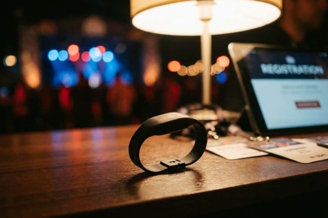 Zwarte RFID polsband op houten registratiebalie bij festival met tablet en badges, publiek wazig op achtergrond