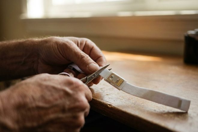 Handen knippen voorzichtig een witte RFID-polsband door met een schaar op een houten bureau