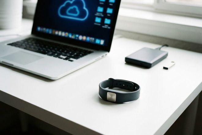 RFID-polsband op wit bureau naast laptop met cloud-opslag iconen en backup-apparaten zoals harde schijf en USB-stick