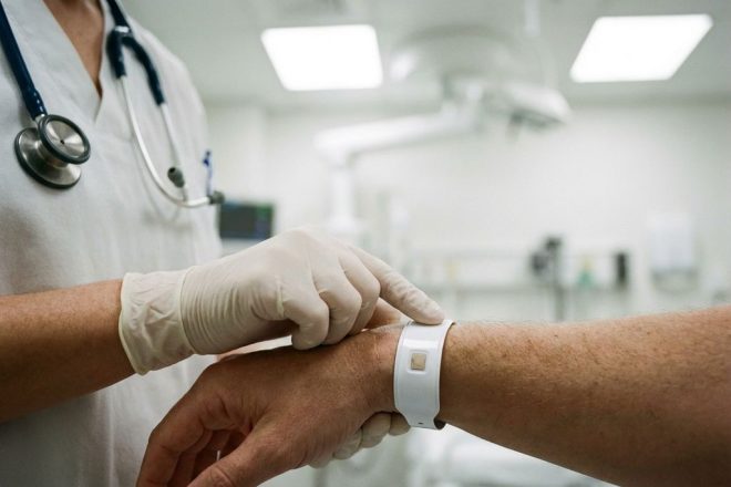 Medisch professional onderzoekt witte RFID-polsband van patiënt in steriele ziekenhuisomgeving