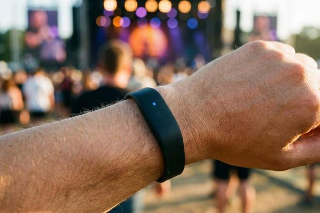 Zwarte RFID polsband met LED-indicator op pols tijdens muziekfestival met kleurrijke achtergrondverlichting