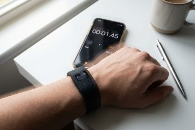 Zwarte RFID-polsband op wit bureau met smartphone die scansnelheid meet, motion blur suggereert snelle technologie