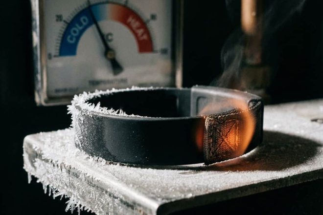 Zwarte RFID polsband op metalen oppervlak met ijskristallen en warmtebestendige materialen, temperatuurmeter op achtergrond
