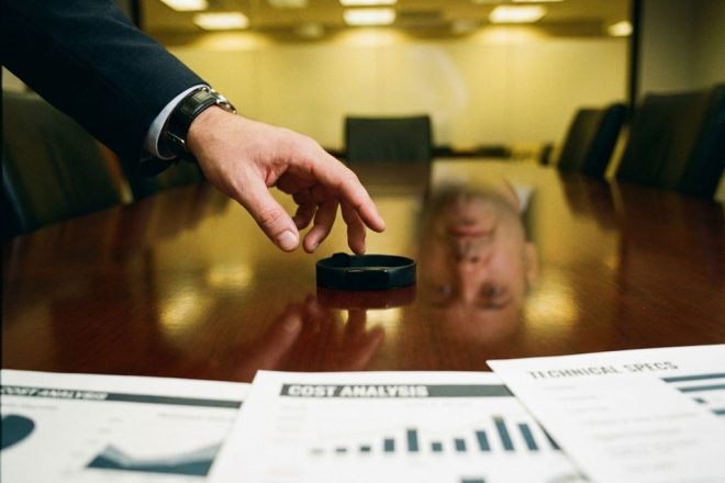 Zakenman overweegt RFID-polsband op vergadertafel met technische documenten en kostenanalyse