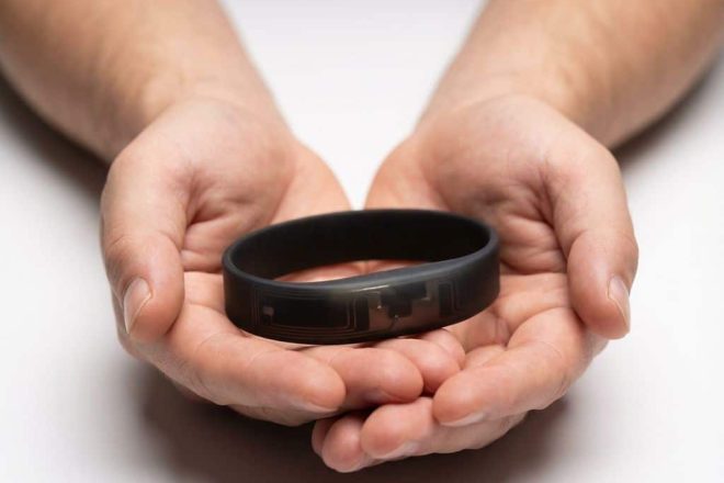 Zwarte RFID polsband van siliconen in handen gehouden tegen witte achtergrond, antennecircuits zichtbaar door materiaal