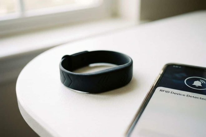 Zwarte RFID-polsband van siliconen op witte ondergrond met smartphone die detectie toont