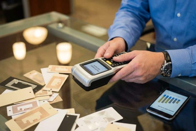 RFID-scanner op glazen bureau met productlabels en smartphone met voorraadgegevens, retailmanager test apparatuur